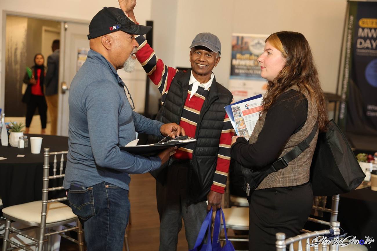 Three attendees talking and exchanging materials at the Training Day Conference