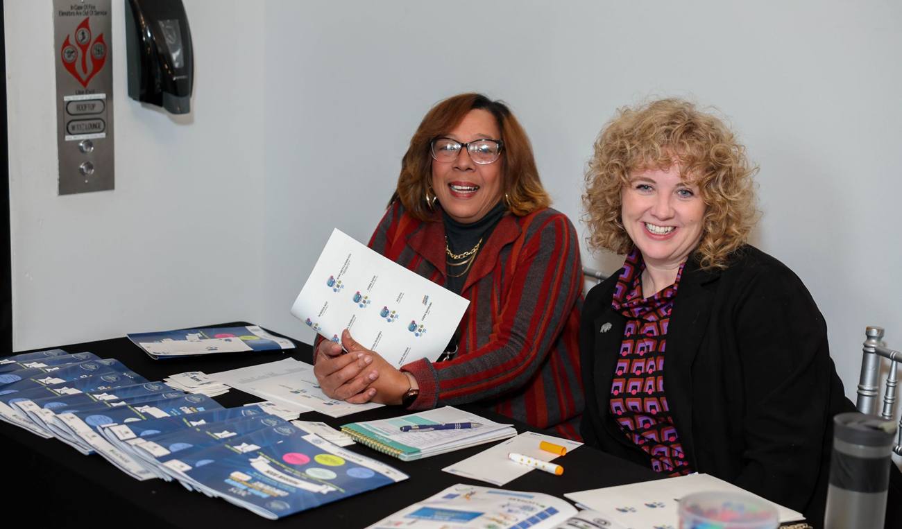 Two smiling volunteers at the conference welcome table