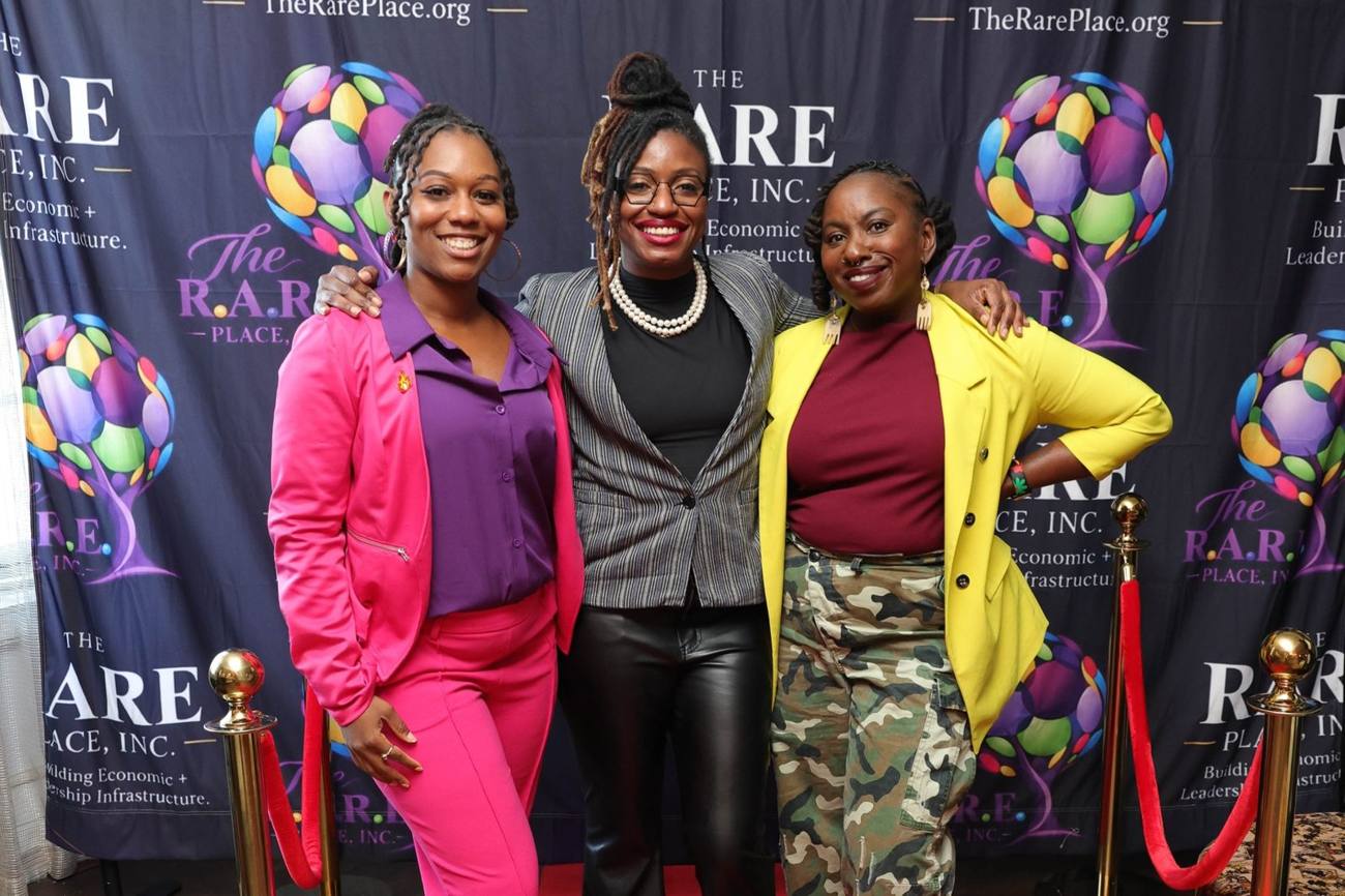 Three cohort members smiling on the red carpet in front of The RARE Place backdrop